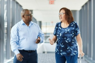 Woman walking with cane walks down hallway talking with man