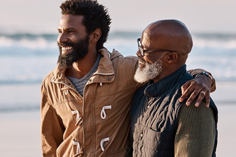 Sons arm around father shoulder while walking on the beach