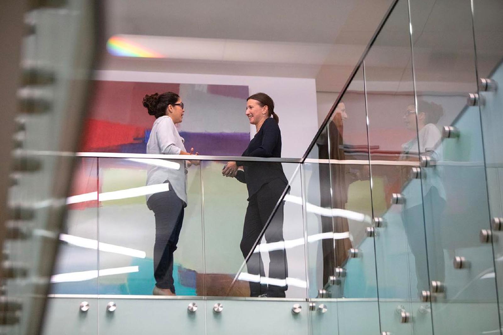 Two women talking by railing in office building