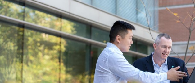 Two male colleagues working on laptop outdoors