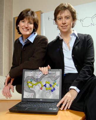Two female colleagues pose with laptop showing computer rendering