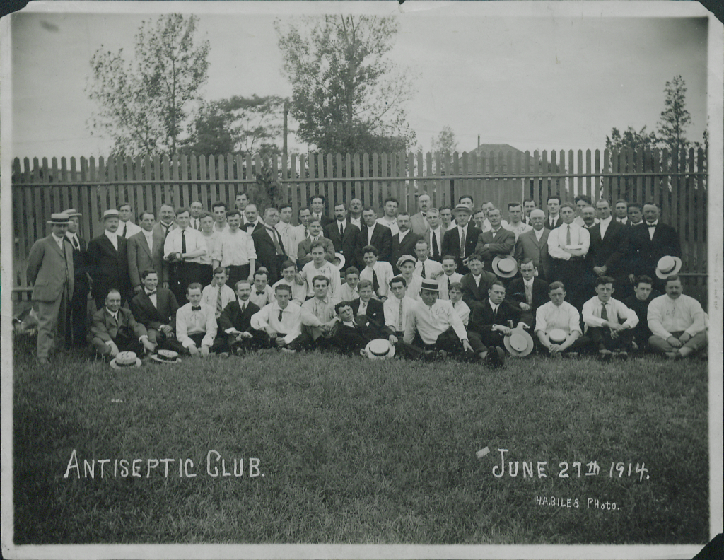 1914 photo of men and women posing in front of fence