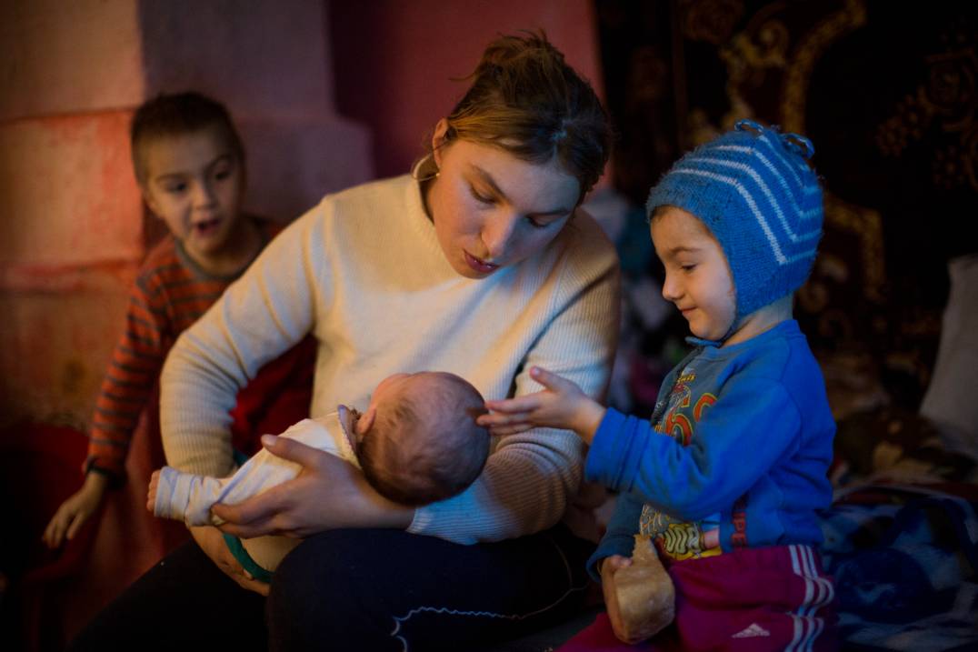 Mother holding baby alongside two other young children - in Romania