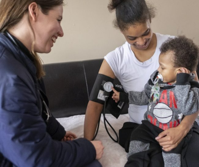 Woman gets her blood pressure checked by nurse while holding her toddler