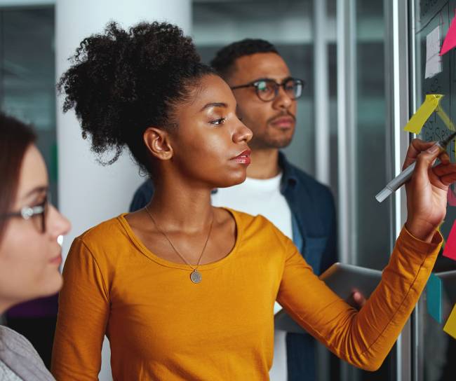 Executives looking at businesswoman writing on adhesive notes stuck over glass