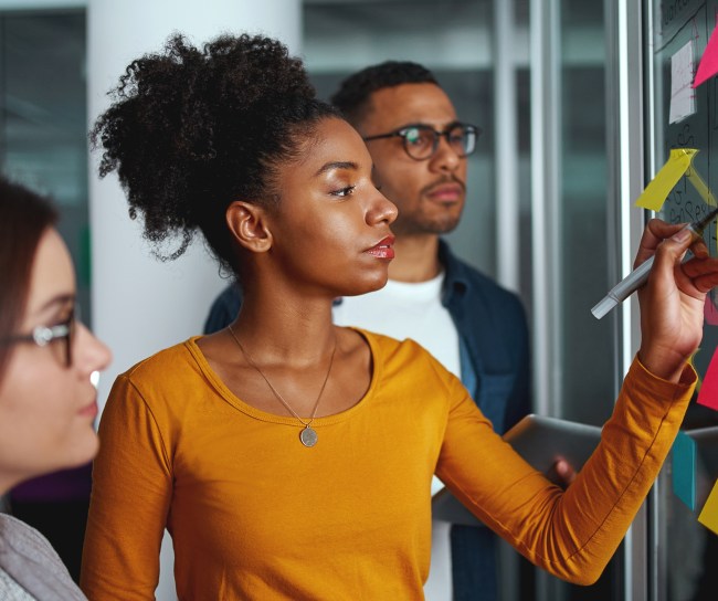 Executives looking at businesswoman writing on adhesive notes stuck over glass
