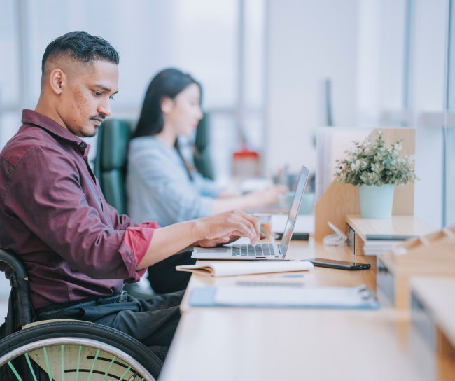 male worker in wheelchair concentrating working in office beside his colleague