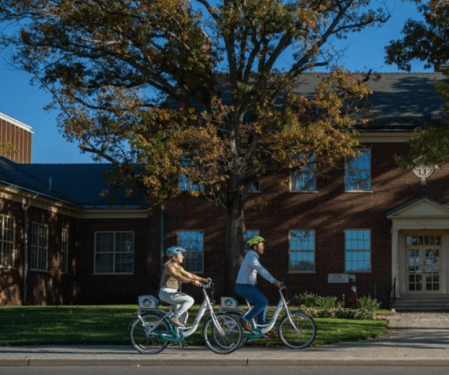 Two employees riding bicycle outside