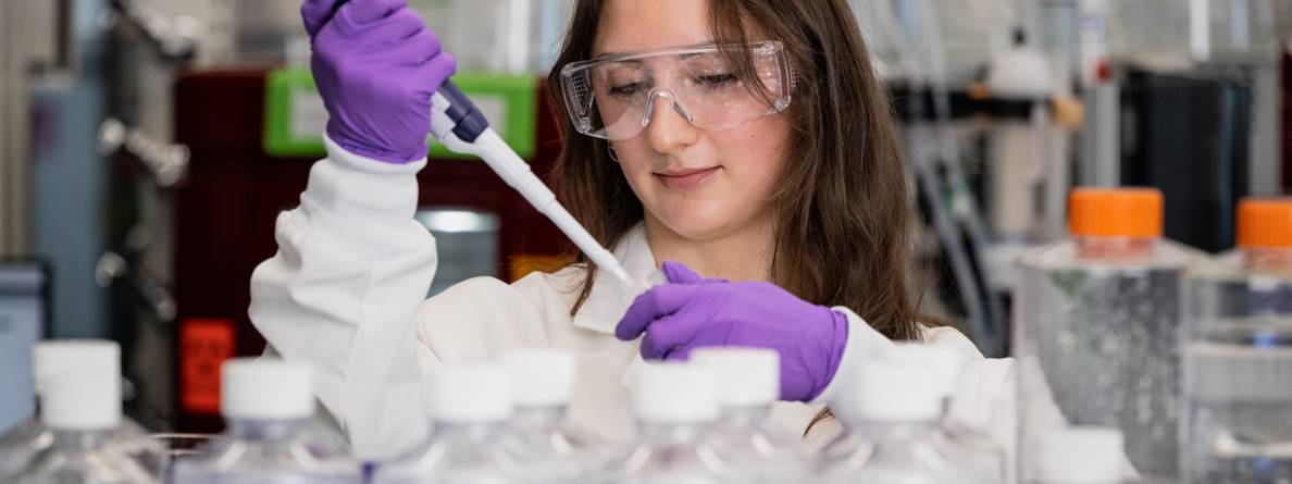 scientist wearing purple gloves and a white coat working in a lab