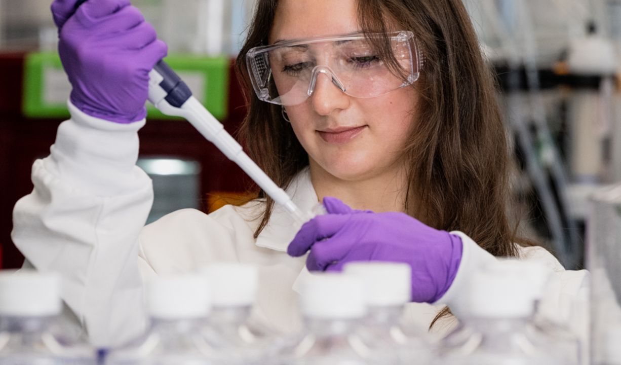 scientist wearing purple gloves and a white coat working in a lab