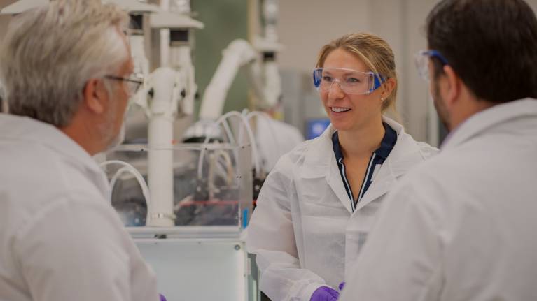 three scientists wearing white lab coats and talking in a lab