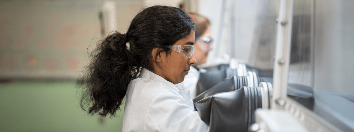 Scientist wearing lab coat and goggles looking in a tube